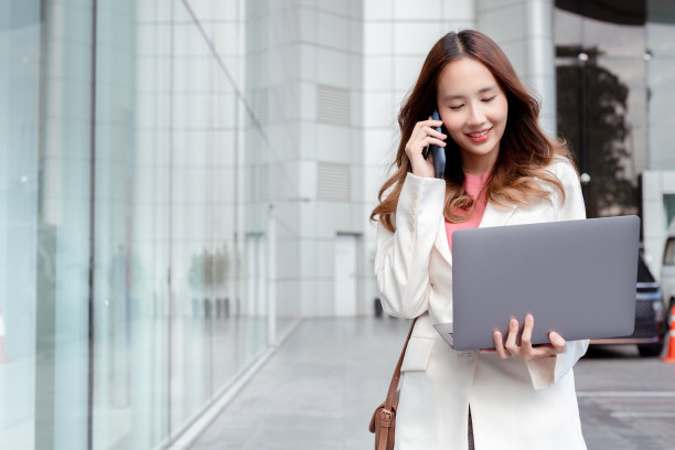 美丽的亚洲女商人拿着笔记本电脑和纸杯热饮，在办公大楼附近的现代化城市里散步享受微笑图片下载