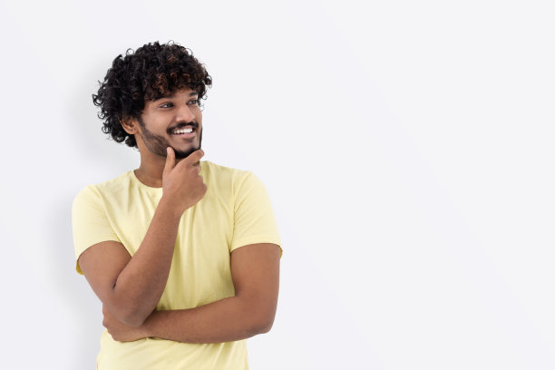 快乐的人看向别处，微笑着思考着什么。带着卷头发的微笑的亚洲男人看着空旷的地方图片下载