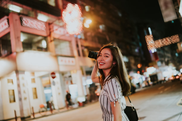 夜晚的香港，在霓虹灯招牌的街道上，年轻的亚洲女子拿着相机在拍照图片下载