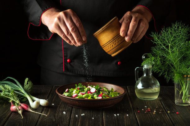 新鲜蔬菜沙拉必须加盐。厨师往盛着美味沙拉的盘子里加盐。节食晚餐或午餐图片下载