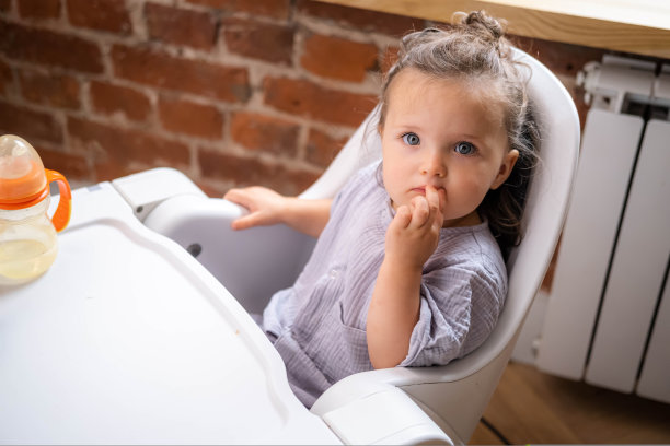 白人女婴，2岁左右，围兜，坐在高脚椅上，从盘子里吃意大利面，孩子自己喂养，婴儿主导的断奶思想，健康营养的固体食物给婴儿。图片下载