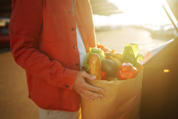 车旁边拿着购物袋的年轻人。图片下载