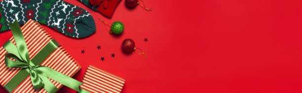 羊毛袜子与圣诞新年的装饰品，礼品盒，球，闪闪发光的五彩纸屑在红色背景上俯瞰平躺。节日概念，圣诞礼物。恭喜背景与文字空间。图片下载
