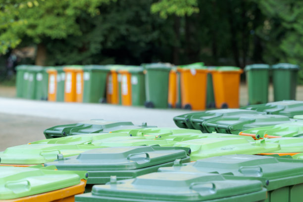 节日活动结束后，公园内摆放着一堆绿色和橙色的废纸塑料垃圾桶图片下载