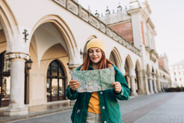 迷人的年轻女游客正在探索新的城市。在克拉科夫市场广场上，戴着帽子的红发女孩手持纸质地图。秋天去欧洲旅游。高质量的照片图片下载