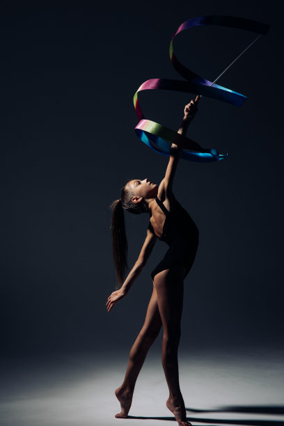 体操小女孩在灯光的照耀下手拿丝带表演体操。图片下载