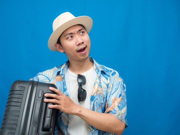 旅游男子戴着帽子拿着行李深思熟虑的仰望蓝色的背景图片下载