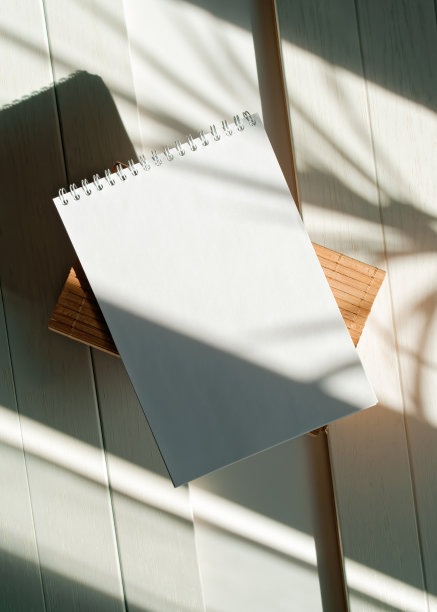 白色桌子上的木箱上放着一本打开的空白记事本。植物的影子落在纸上。记事本模型。窗户射进来的自然光。前视图。平的。副本的空间。图片下载