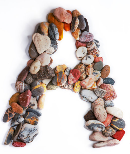 在白色孤立的背景上用光滑的石头刻出的字母。河边的石头上排列着一个字母，细节，特写。有选择性的重点图片下载