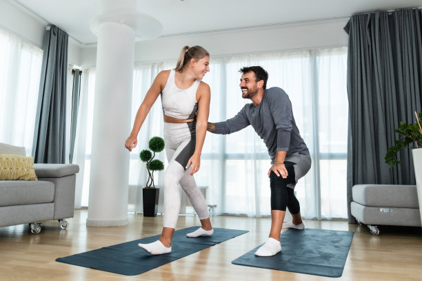 年轻的积极的夫妇在他们的家里锻炼瑜伽垫伸展他们的肌肉。妻子和丈夫通过锻炼来减轻一天工作后的压力。图片下载