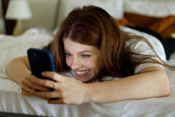 微笑的女孩在床上用智能手机。睡觉前交流，社交网络。图片下载