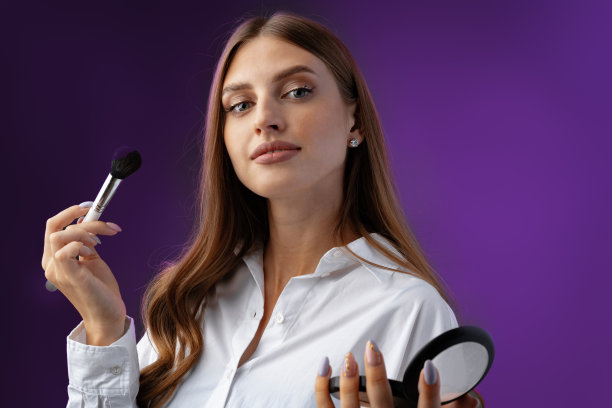 年轻女子与化妆手持粉刷在紫色的背景图片下载