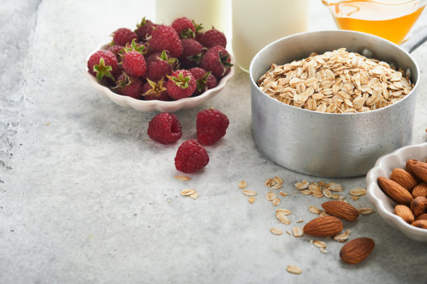 在灰色混凝土旧桌子背景上，用燕麦、牛奶、覆盆子、蜂蜜和杏仁做燕麦片或格兰诺拉麦片的配料。健康早餐的食材。图片下载