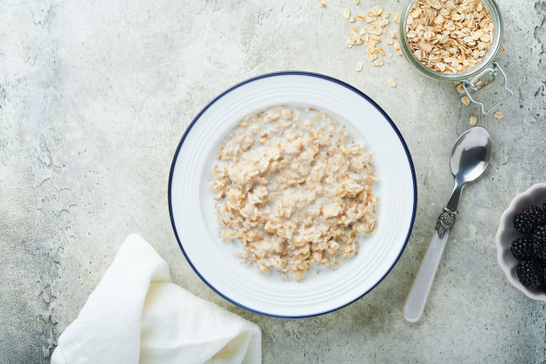 燕麦片。复古浅灰色蓝绿色的桌子上，一碗燕麦粥配草莓、杏仁和牛奶。平铺风格的俯视图。天然成分。热而健康的早餐和减肥食品。图片下载