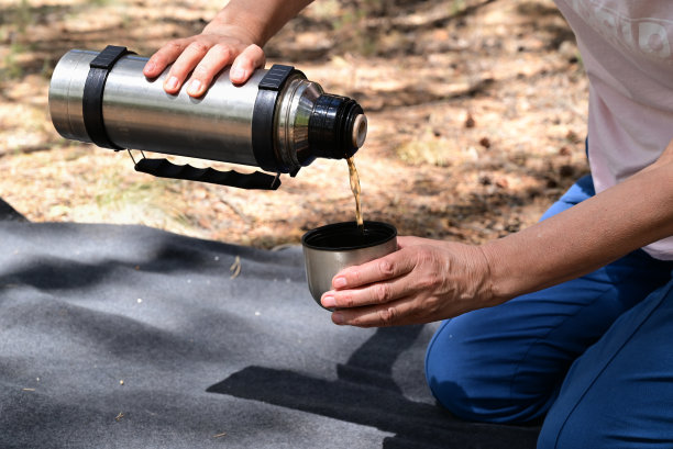 野餐时，森林里妇女的手从保温瓶里倒茶图片下载