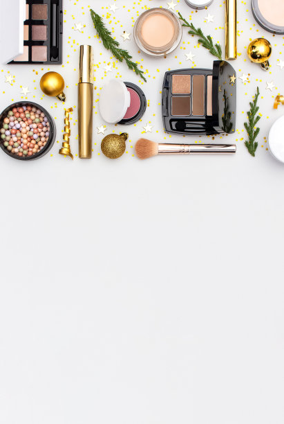 化妆，睫毛膏，粉底霜，口红，眼影，腮红球和新年装饰品，金色的圣诞球，五彩纸屑，星星，杉木树枝，在浅色背景平铺俯视图。化妆品、节日圣诞节图片下载