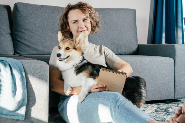 卷发高兴，快乐的赤脚妇女与狗柯基坐着，放松和看书的室内地毯图片下载