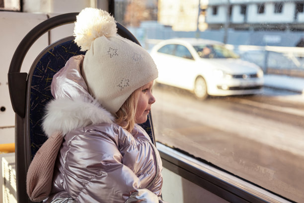 小女孩坐在公共交通的窗口，看着窗口。小孩在都市交通工具里，坐在座位上，微笑着。公共交通与城市生活方式的概念。本空间图片下载