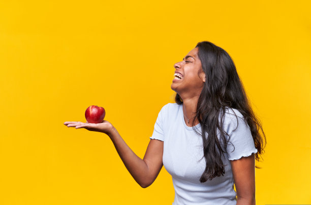 快乐的独立照片，印度女士拿着苹果，笑着。黄色背景，有复制空间。图片下载
