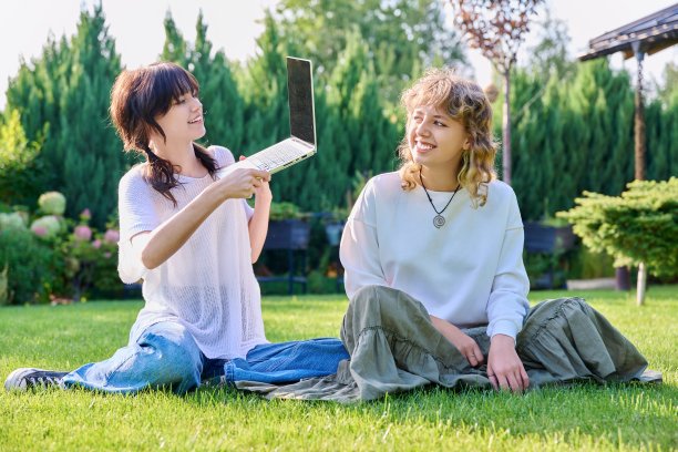 十几岁的女学生朋友坐在草地上笑着拿着笔记本电脑图片下载