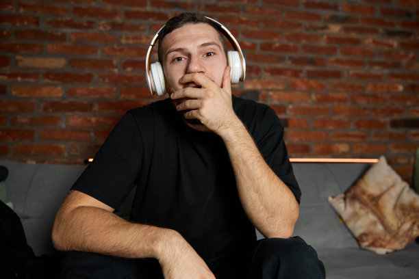 英俊的大胡子戴着耳机在家听音乐。音乐。半身像，年轻的小伙子微笑着，穿着休闲的青春风格的衣服，坐在沙发上。情绪的概念,图片下载