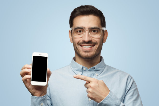 穿着蓝色背景衬衫的男子展示手机，手指指向黑色的复制空间屏幕图片下载