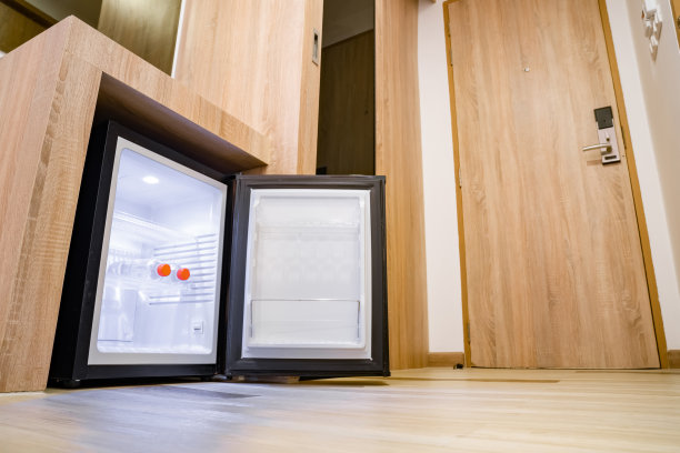 酒店房间里木制柜台下面的小冰箱和两个水瓶。这款极简风格的冰箱有黑白两色，配有LED，里面有3个搁板。图片下载