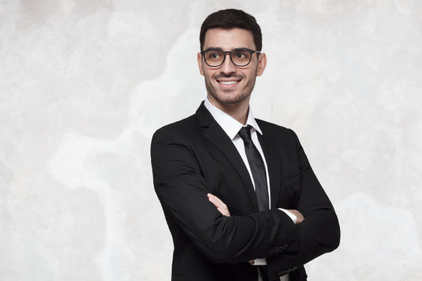 商人被隔离在灰色的背景中，穿着正装，戴着眼镜，双臂交叉，微笑着图片下载