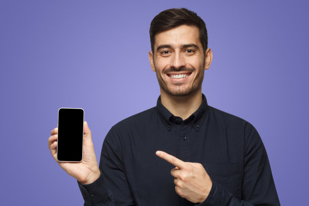 年轻英俊的微笑男子拿着和展示与手指空白的智能手机与广告的copyspace图片下载