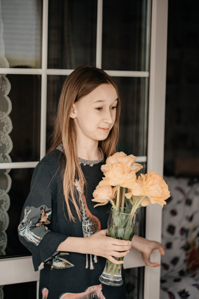 这个女孩并不掩饰自己的情绪。一个小女孩手里拿着一个花瓶。阳台上一个孩子拿着花的照片。春天的照片与一个婴儿和鲜花。图片下载