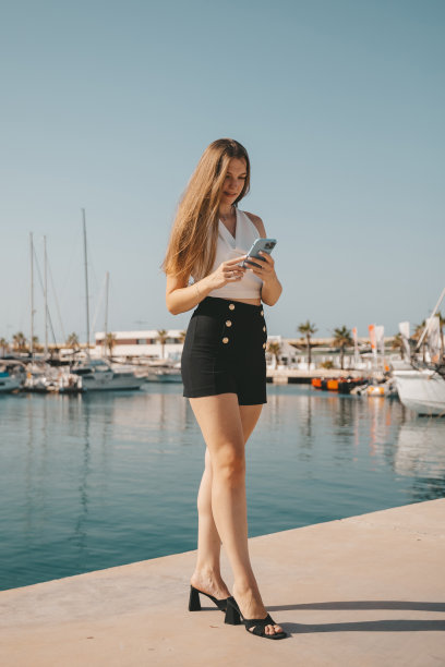 美丽的女人在蓝色的大海和游艇的背景下打电话图片下载