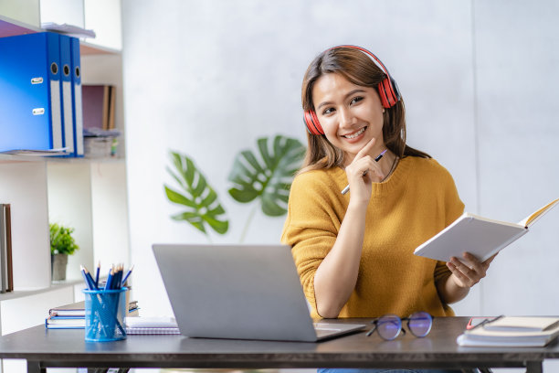 一名年轻女子戴着耳机，用笔记本电脑学习和上网。图片下载