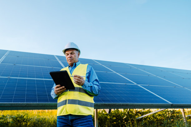 工程师站在太阳能电池板前。手持平板，检查光伏太阳能电池板。图片下载