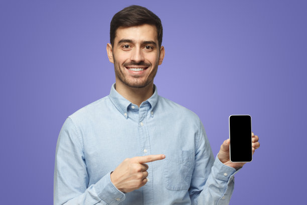 紫色背景的蓝衬衫男子，展示的智能手机指向空白屏幕图片下载