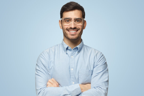 英俊微笑的商人在蓝色衬衫交叉双臂站在蓝色背景图片下载