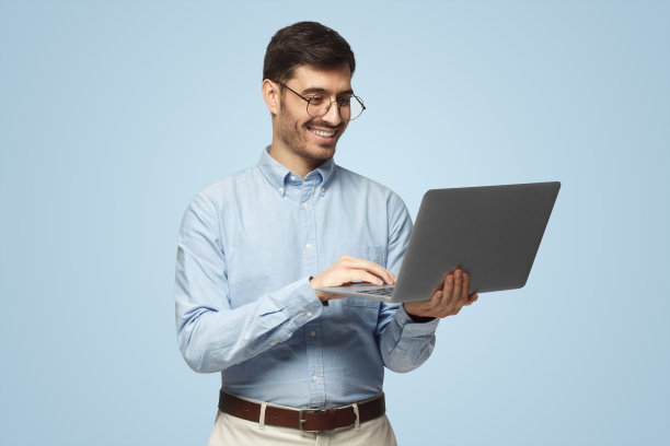 画像年轻英俊的男老师在衬衫拿着笔记本电脑和微笑，孤立的蓝色图片下载