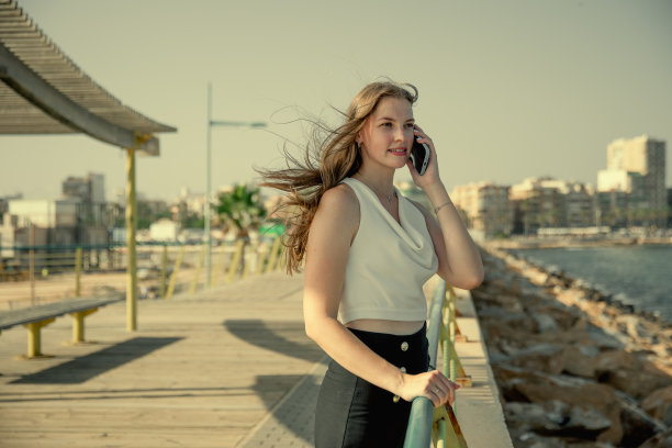一名年轻时尚的女子在城市海景的背景下用智能手机交流图片下载