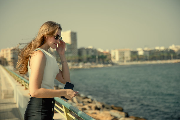 一名年轻时尚的女子在城市海景的背景下用智能手机交流图片下载