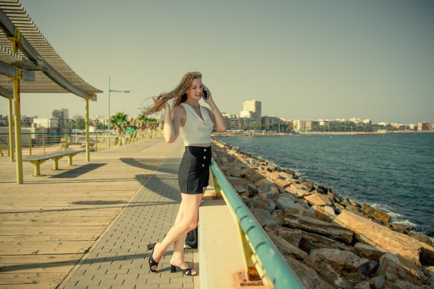 一名年轻时尚的女子在城市海景的背景下用智能手机交流图片下载