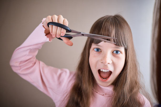 一个有雀斑和蓝眼睛的小女孩用剪刀剪她的头发。图片下载