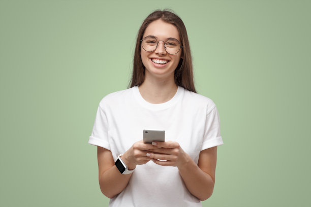 戴着透明眼镜的美丽女孩在电话上交换信息，在绿色上与世隔绝图片下载