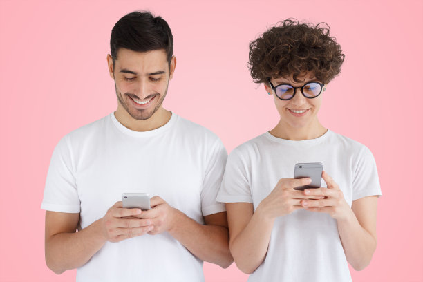 年轻的情侣拿着智能手机，肩并肩站在粉色的大地上图片下载