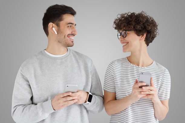 年轻幸福的夫妇肩并肩站在一起，用智能手机看着对方图片下载