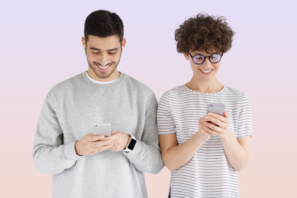 年轻幸福的夫妇拿着手机，肩并肩站在粉色的背景下图片下载