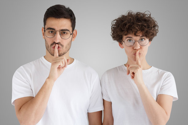 在灰色的背景下，年轻的夫妇做着沉默的手势图片下载