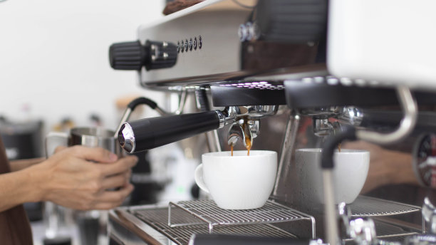 咖啡师用咖啡机制作艺术拿铁。专业的现代化浓缩咖啡机将热饮倒入杯中。咖啡馆里的概念咖啡。图片下载