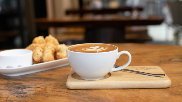 一杯白色的艺术拿铁加卡布奇诺咖啡和油炸油条配蒸蛋奶沙司，放在咖啡馆的桌子上。在杯子上放泡沫花。关闭咖啡杯在木桌上。图片下载