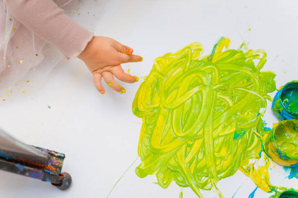 一个小女孩把手指伸进绿色颜料里。孩子用黄色水粉的手在一片白色的叶子上画画图片下载