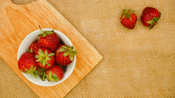 新鲜的草莓放在玻璃碗里平放在砧板上图片下载