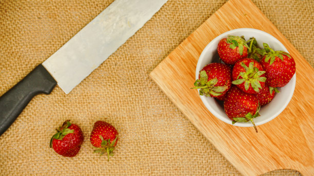 新鲜草莓放在玻璃碗里，用刀平放在砧板上图片下载